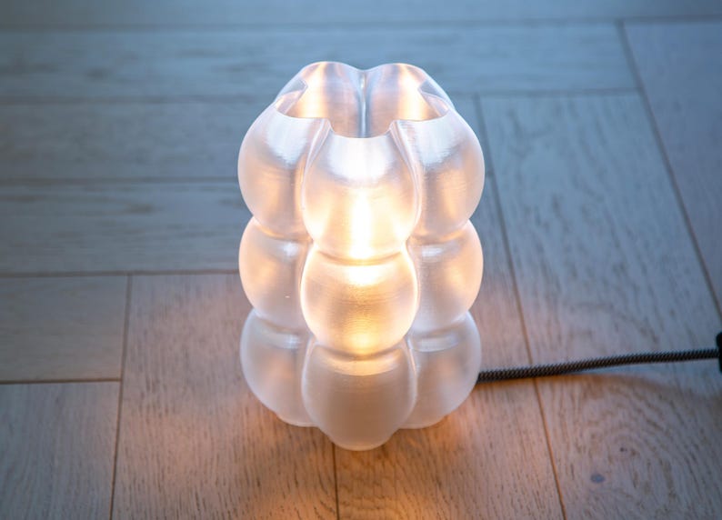Yoli: Luminária de mesa, cabeceira e escrivaninha moderna. Luz ambiente, original e suave. Disponível em rosa, vermelho, azul, verde, roxo e amarelo, com formato ondulado. Fabricada no Reino Unido. Transparente