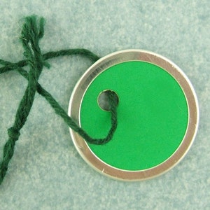 May include: A green tag with a silver rim and a hole in the center. The tag is attached to a green string.