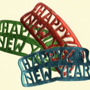 May include: Three colorful felt banners with the words "HAPPY NEW YEAR" cut out. The banners are in green, red, and blue, and are slightly overlapping. The background is a light cream color.