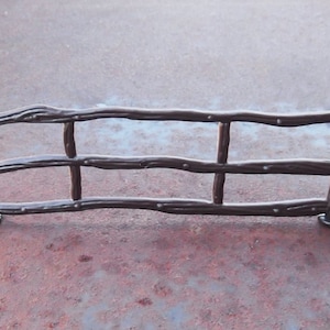 May include: A decorative, dark brown metal fence with a rustic design. The fence has horizontal rails and vertical posts, with small rivet details. The overall design evokes a rural or farmhouse aesthetic.