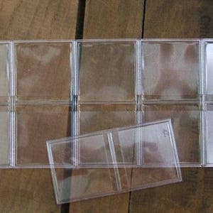 May include: Clear plastic coin holder with multiple compartments, designed to hold and display coins. The holder is rectangular and has a hinged design, allowing it to fold open and closed. The background is a wooden surface.