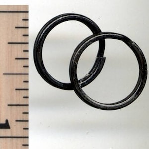 Könnte beinhalten: Zwei ineinandergreifende, dunkelgraue Metallringe. Die Ringe sind kreisförmig und scheinen aus einem robusten Material zu bestehen. Das Bild enthält ein Lineal zum Maßstab, das zeigt, dass die Ringe etwa 2,5 cm Durchmesser haben.