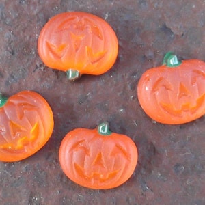 May include: Four orange pumpkin-shaped sweets with a carved jack-o'-lantern face. The sweets are on a brown surface.