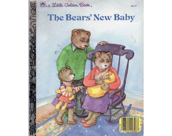 May include: A Little Golden Book titled "The Bears' New Baby" depicts a family of brown bears. The mother bear is rocking in a chair, holding a baby bear. The father bear is standing behind the mother bear, and a young bear is standing in front of the mother bear. The book cover is illustrated with a light blue background and a light blue and white patterned rug.