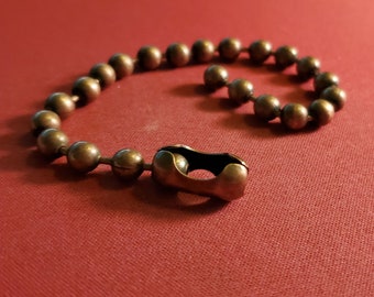 May include: A brass chain with a clasp, made of round beads. The chain is lying on a red surface.