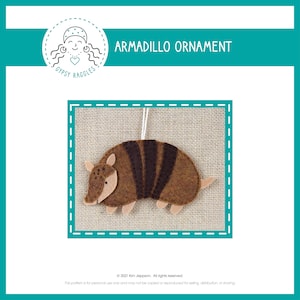 May include: A felt armadillo ornament with brown and black stripes. The ornament is hanging from a string and is on a hessian background. The text "ARMADILLO ORNAMENT" is at the top of the image.
