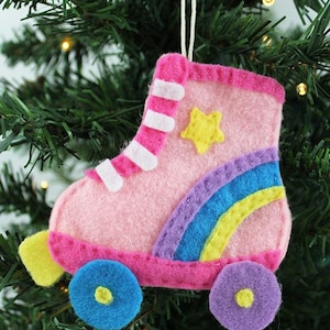 May include: A pink felt roller skate Christmas ornament with white stripes, a yellow star, and a rainbow design. The wheels are blue and purple. The ornament hangs from a white string.