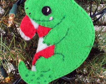 May include: Green felt Christmas ornament shaped like a lizard holding a candy cane. The candy cane is red and white with white beads sewn on.