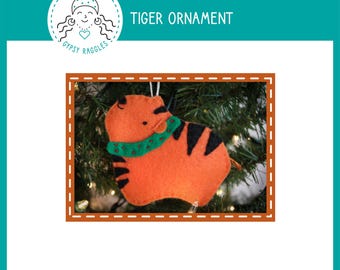 May include: A felt tiger ornament with orange fur, black stripes, and a green collar. The ornament is hanging on a Christmas tree.
