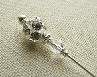 May include: A silver pin with a clear crystal bead and a round, sparkly, rhinestone top.