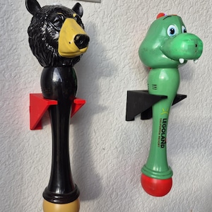 May include: Two novelty bubble wands. One is a black bear with a yellow nose and a black body. The other is a green alligator with the text "LEGOLAND CALIFORNIA RESORT" on the body. Both are mounted on the wall.