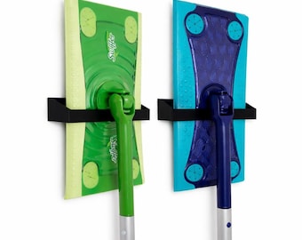 May include: Two Swiffer mops, one green and one blue, mounted on a white wall. The green mop has a green handle and a yellow and green cleaning pad. The blue mop has a blue handle and a blue and turquoise cleaning pad. Both mops are held in place by black metal brackets.
