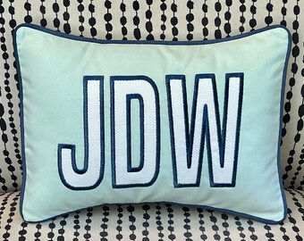 May include: A light blue pillow with a navy blue trim and the letters JDW embroidered in white with a navy blue outline.