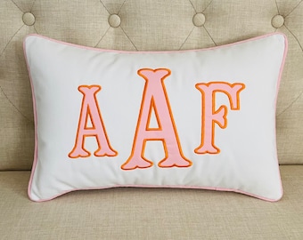 May include: White pillow with pink and orange embroidered letters spelling "AAF".