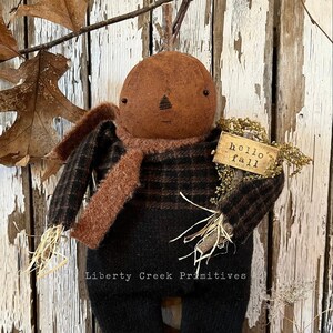 May include: A brown and black striped scarecrow doll with a pumpkin head and a sign that says "hello fall".