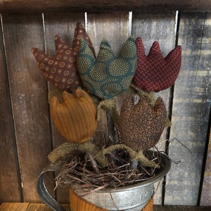 May include: A rustic floral arrangement featuring fabric tulips in shades of brown, green, and burgundy. The flowers are arranged in a galvanized metal container with a decorative orange ribbon. The arrangement is a charming home decor piece.