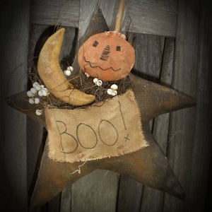 May include: A rustic Halloween star decoration with a pumpkin and crescent moon. The star is brown with a burlap banner that reads "BOO!". The pumpkin has a stitched face. The moon and pumpkin are tan and orange.