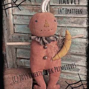 May include: A 14 inch primitive pumpkin doll pattern called "Harvey" by Liberty Creek Primitives. The doll is made of brown fabric and has a brown fabric stem. The doll is holding a yellow crescent moon.