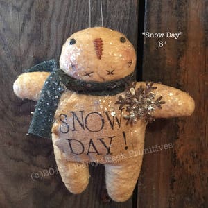 Könnte beinhalten: Ein handgemachtes Filz-Schneemann-Ornament mit einem Juteschild "Snow Day!" , einem grünen Schal und einer glitzernden Schneeflocke. Das Ornament ist 15 cm hoch.