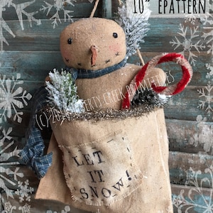 以下が含まれることがあります： 赤いキャンディーケーン、青い格子柄のスカーフ、そして「LET IT SNOW!」と書かれた麻袋を持った、高さ25cmの麻の雪だるま人形。人形は青い木製の背景に白い雪片が描かれたフックに吊るされています。