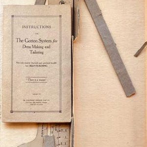 Puede incluir: Un folleto de instrucciones vintage Gorton System for Dress Making and Tailoring, una escuadra de sastre de cartón, una herramienta curva para trazar patrones, un lápiz azul pequeño y una tira de papel rosa con la palabra FAVORITE en una caja.