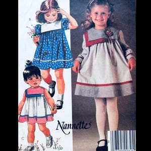 Puede incluir: Patrón de costura de vestidos infantiles vintage con tres diseños de vestidos. Los vestidos incluyen un vestido floral azul, un vestido rosa y blanco y un vestido gris con ribete rojo. El patrón está etiquetado como "Nannette".