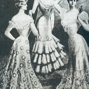 May include: Three women in vintage dresses with ruffled skirts and elaborate hairstyles. The women are standing in a studio setting and are looking at the camera.