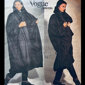 May include: A vintage Vogue Patterns sewing pattern featuring a black hooded cape. The image shows a woman wearing the cape, with the Vogue logo and pattern details visible. The pattern includes the text "CO-ALIN FABRIC SHOP #724".