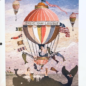 May include: A colorful, embroidered artwork featuring a hot air balloon with the text "SIREN'S HAND LAUNDRY". The balloon is above a whale with mermaids and other figures. The image is from the "Hooking Artists" newsletter.