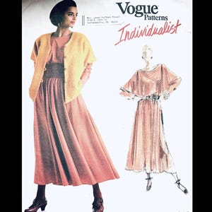 May include: Vogue Patterns Individualist fashion sewing pattern. The image shows a woman wearing a peach-colored dress with a yellow cardigan and a black hat. The pattern includes a sketch of a similar dress. The text on the pattern reads "Vogue Patterns Individualist".