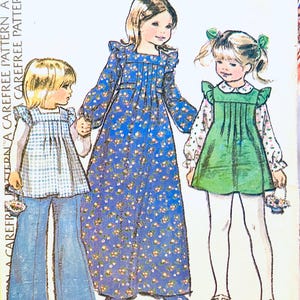 Könnte beinhalten: Eine Schnittmuster-Umschlagillustration mit drei Kindern in verschiedenen Outfits: ein blaues Vichy-Karo-Oberteil mit Schlaghose, ein langes blaues Blumenkleid mit gerüschten Schultern und ein grüner Trägerrock über einem geblümten Langarmshirt.