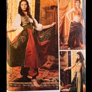 May include: A woman wearing a red and green costume with a long skirt and a vest. The costume is decorated with paisley patterns. The woman is standing on a patterned rug.