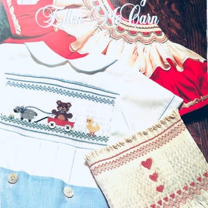May include: A instructional book titled Picture Smocking with Ellen McCarn featuring a white garment with smocked bear, wagon, and duck embroidery, a red and cream smocked garment, and a cream fabric swatch with red heart embroidery patterns.
