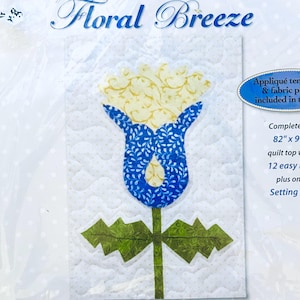 May include: A floral quilt block kit featuring a stylized flower design. The flower has a blue patterned bloom with a yellow center and green leaves. The text "Floral Breeze" is at the top.