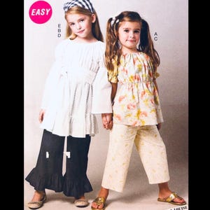 May include: A sewing pattern illustration featuring two outfits. One outfit includes a white long-sleeved tunic with a tie waist and black flared trousers with ruffled hems. The second outfit features a floral print top with puff sleeves and matching cropped trousers.