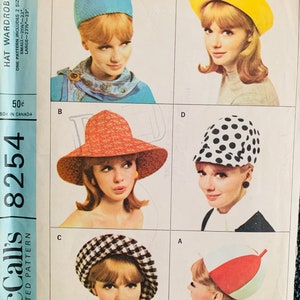 May include: A vintage sewing pattern for a hat wardrobe. The pattern includes instructions for making five different hats: a blue cloche hat, a yellow beret, a red and white sun hat, a black and white polka dot hat, and a red, white, and green hat. The pattern is for sizes small and large.