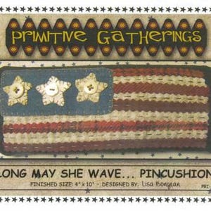 May include: A handcrafted pincushion in the shape of an American flag. The flag features a blue field with three star-shaped buttons and red and white striped sections. The text "Primitive Gatherings" and "Long May She Wave... Pincushion" are displayed.