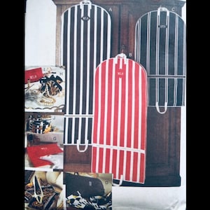 May include: Three garment bags with vertical stripes in black and white, red and white, and black and dark green. Each bag has a handle and a monogram. Other items include a red box, a black bag, and a decorative box.