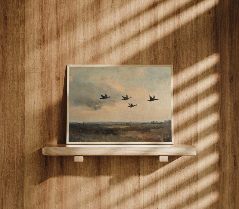 K&ouml;nnte beinhalten: Ein gerahmtes Gem&auml;lde, das eine Landschaft mit f&uuml;nf V&ouml;geln zeigt, die in Formation vor einem bew&ouml;lkten Himmel fliegen. Das Gem&auml;lde befindet sich auf einem Holzregal an einer Holzvert&auml;felung.