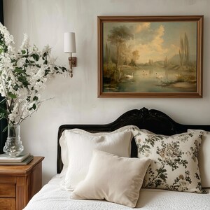 K&ouml;nnte beinhalten: Ein wei&szlig;es Bett mit einem schwarzen Kopfteil und wei&szlig;en Bettw&auml;sche. Auf dem Bett liegen mehrere Kissen, darunter ein Kissen mit Blumenmuster und ein schlichtes wei&szlig;es Kissen. &Uuml;ber dem Bett h&auml;ngt ein Gem&auml;lde mit einer Seenszene.
