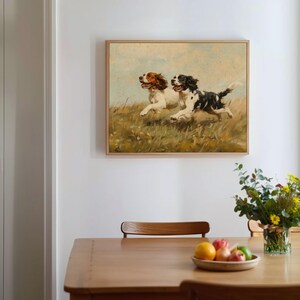 May include: A vintage painting of two Springer Spaniel dogs running through a field of tall grass. The dogs are white with brown and black markings. The painting is framed in a light wood frame.