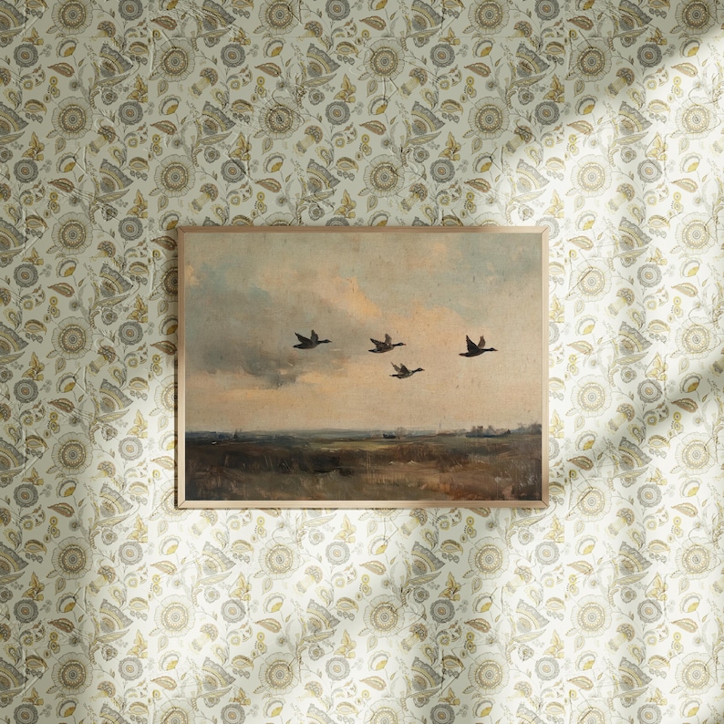 K&ouml;nnte beinhalten: Ein gerahmtes Gem&auml;lde einer Landschaft mit f&uuml;nf G&auml;nsen, die in Formation vor einem bew&ouml;lkten Himmel fliegen. Das Gem&auml;lde ist vor dem Hintergrund einer floralen Tapete mit einem sich wiederholenden Muster aus kleinen Blumen und Bl&auml;ttern platziert.