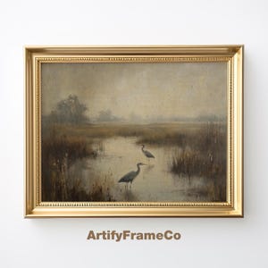 Puede incluir: Una pintura enmarcada de un paisaje brumoso con tres garzas grises de pie en un cuerpo de agua poco profundo. La pintura está en un marco dorado.