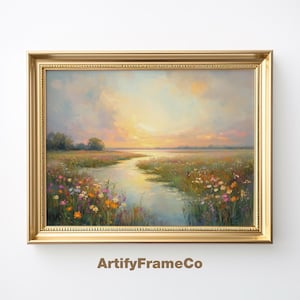 Puede incluir: Una pintura enmarcada de un paisaje con un río serpenteando a través de un campo de flores silvestres. El cielo es de un azul suave con nubes y el sol se pone en la distancia. La pintura está en un marco dorado.