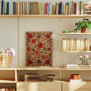 May include: A framed floral print with red flowers and green leaves. The print is displayed on a light-colored wall, surrounded by wooden shelves filled with books and decorative items. A woven basket with flowers is on a shelf.