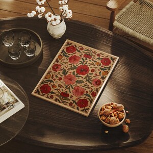 May include: A wooden coffee table with a floral patterned tray, a small bowl of nuts, and a tray of glasses. A vase with white flowers sits on the table. The tray features red and pink flowers.