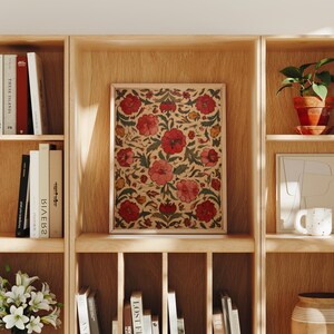 May include: A framed floral print featuring red and pink flowers with green leaves on a beige background. The artwork is displayed in a wooden bookshelf with books, a potted plant, and decorative items.