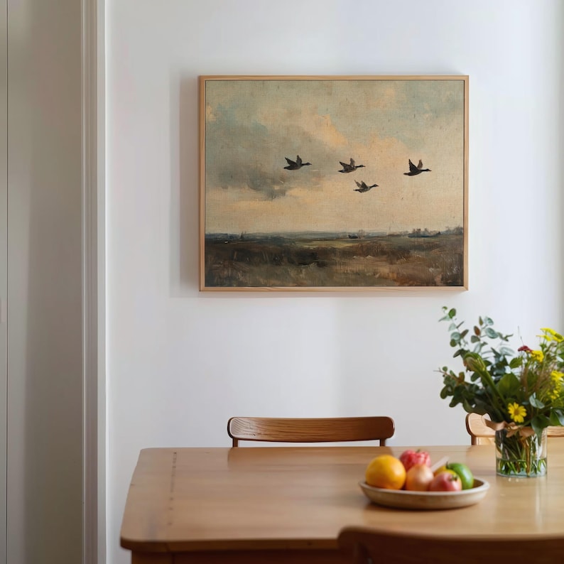 K&ouml;nnte beinhalten: Ein gerahmtes Gem&auml;lde einer Landschaft mit f&uuml;nf Enten, die in Formation &uuml;ber einem bew&ouml;lkten Himmel fliegen. Das Gem&auml;lde ist in einem hellen Holzrahmen gefasst und h&auml;ngt an einer wei&szlig;en Wand.