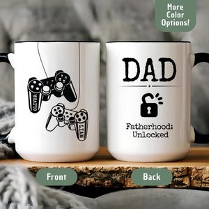 May include: White 15 oz ceramic mug with black handle and rim. One side features a black controller graphic with the name "Oliver", the other side says "DAD" with a lock graphic and "Fatherhood: Unlocked".