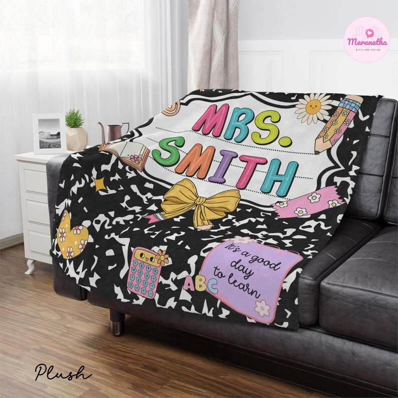 May include: A plush blanket with a black and white notebook paper design. The blanket features the text "MRS. SMITH" in colorful letters, along with school-themed illustrations like a pencil, calculator, and a bow. The phrase "It's a good day to learn" is also included.